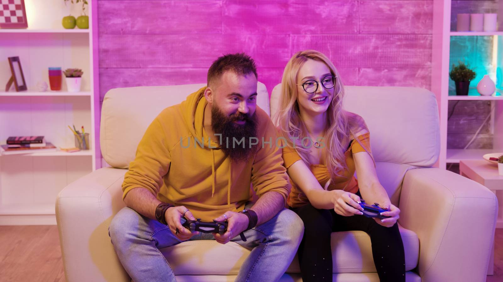 Female gamer playing online video games with her boyfriend sitting on sofa using wireless controllers.