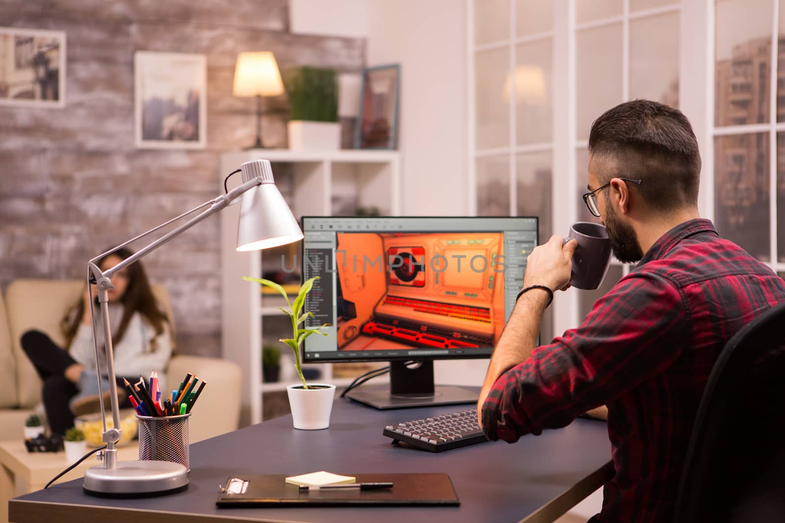 Man taking a sip of coffee while playing video games. Girlfriend relaxing on sofa in the background.