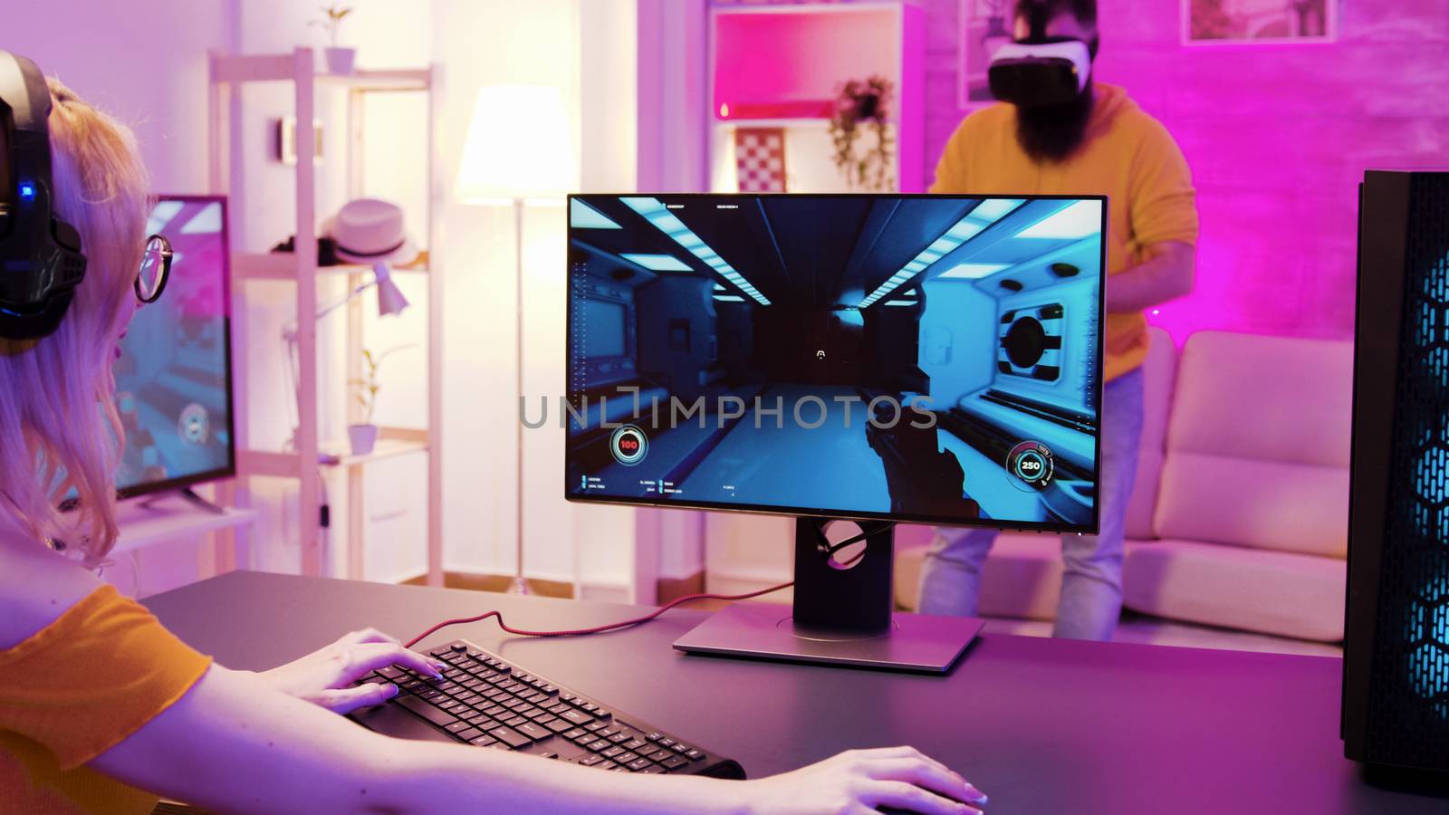 Girl wearing headphones and sitting on gaming chair while playing shooter games. Her partner is wearing virtual reality goggles.