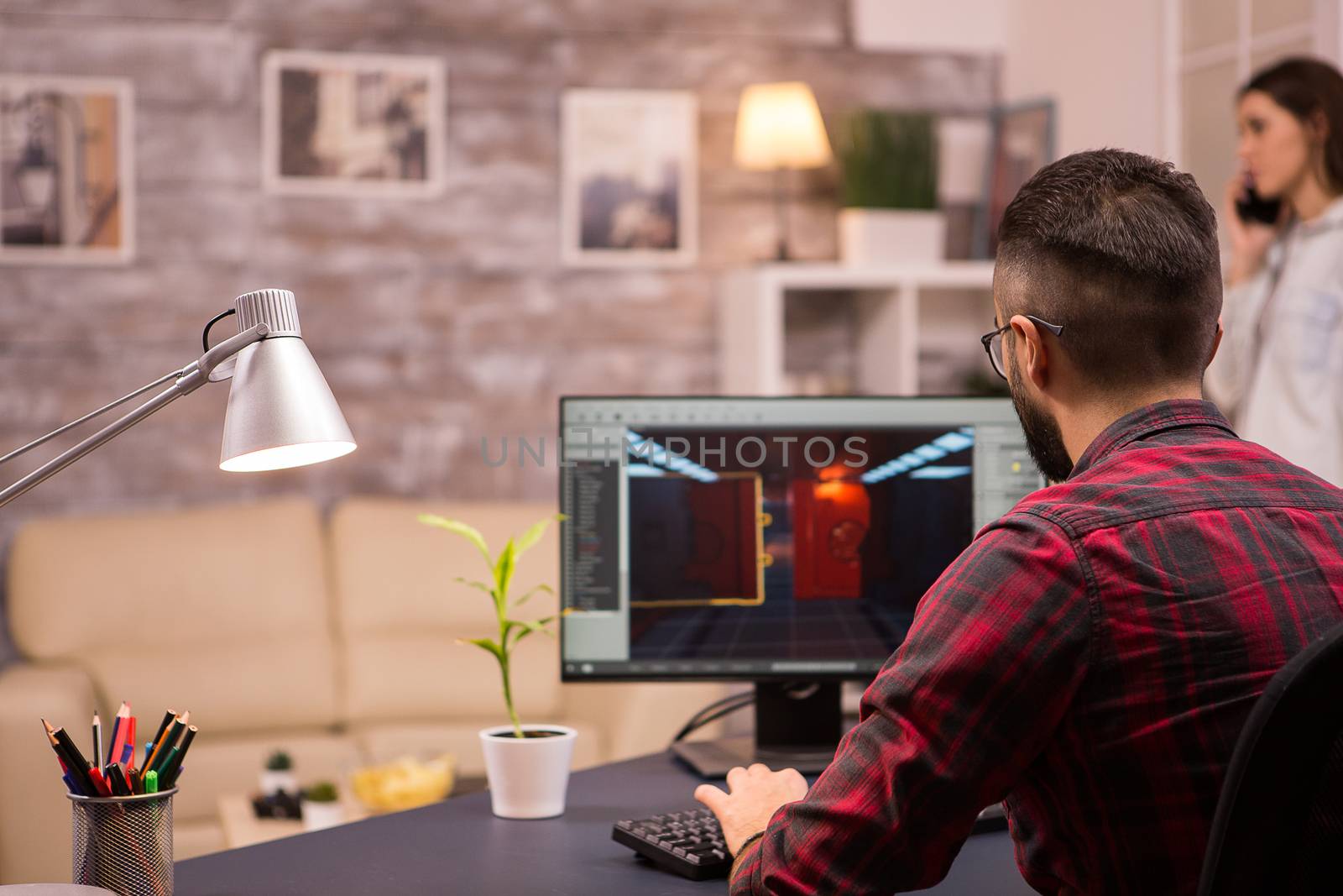 Back view of caucasian man playing video games on home computer. Girlfriend in the background