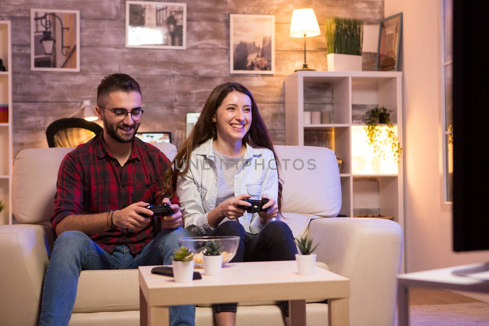 Young couple having fun while playing video games on television sitting on couch at night.