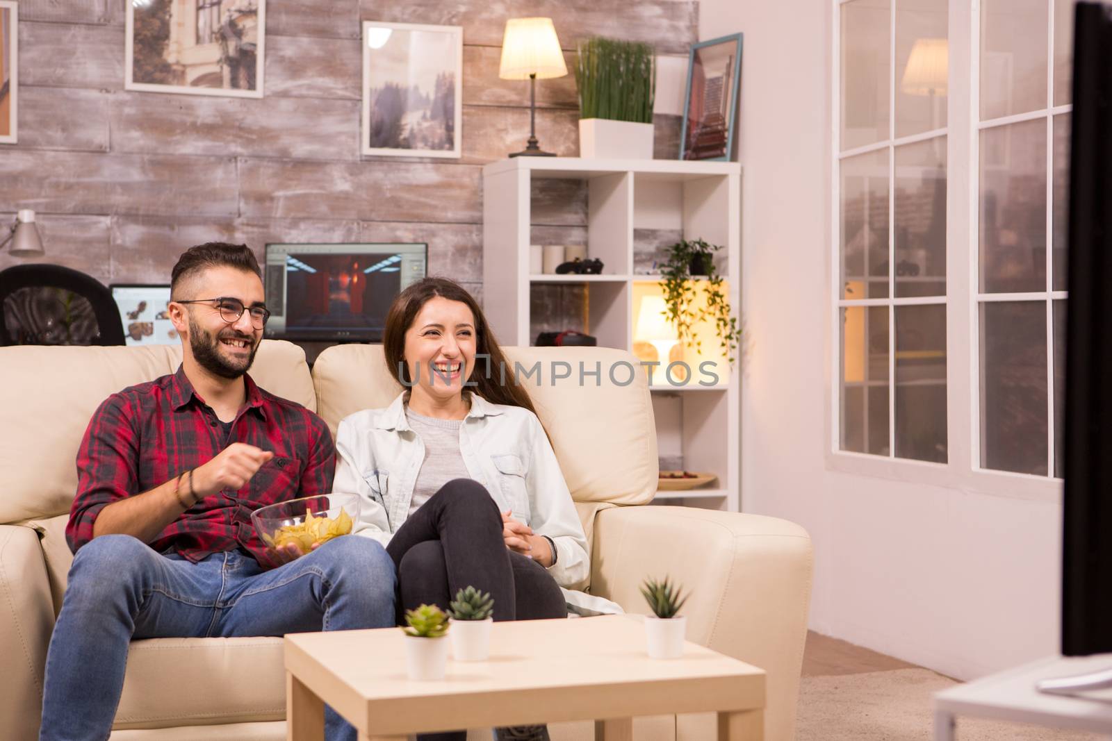 Couple laughing so hard while watching a movie on tv by DCStudio