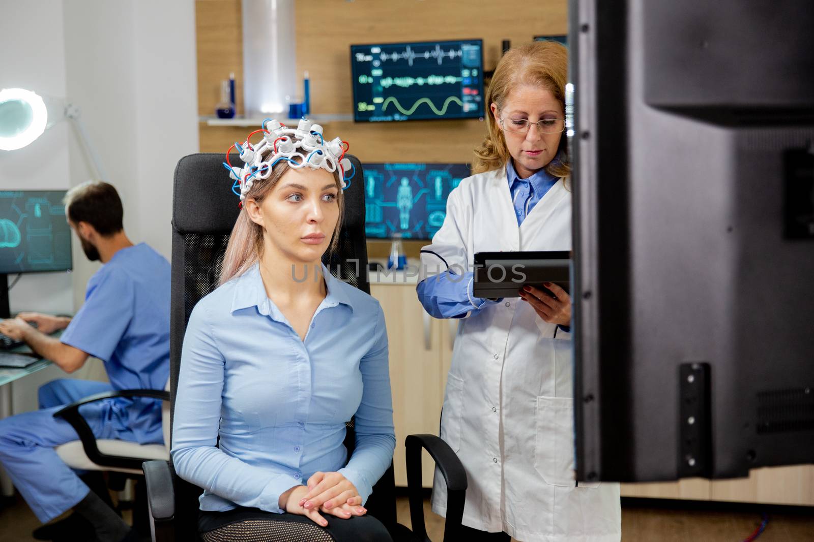 Patient woman with scanning device on her head and doctor scheduling it with tablet in hand. Neurological clinic