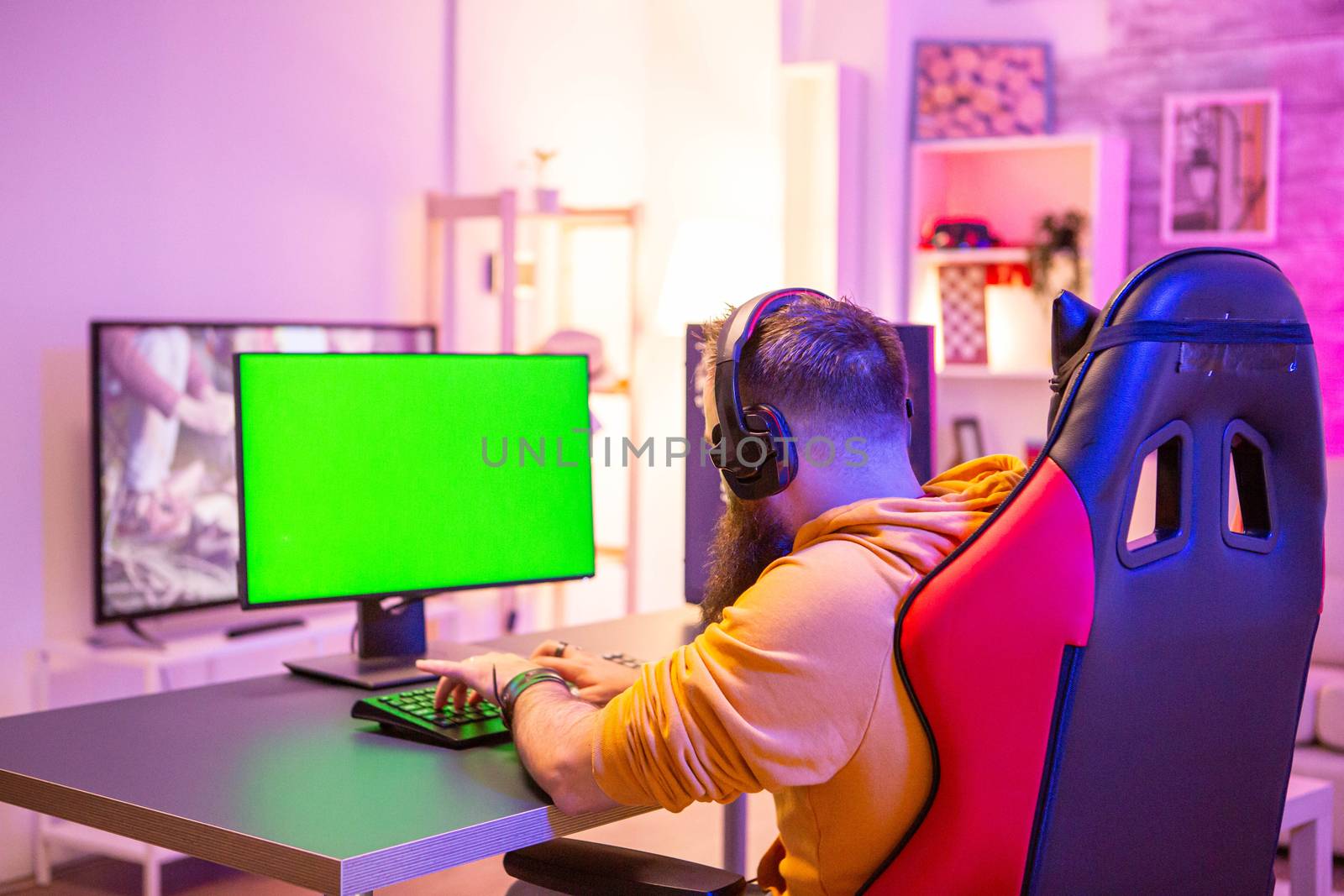 Man playing on powerfull gaming pc in a room with neon lights on a green screen computer.