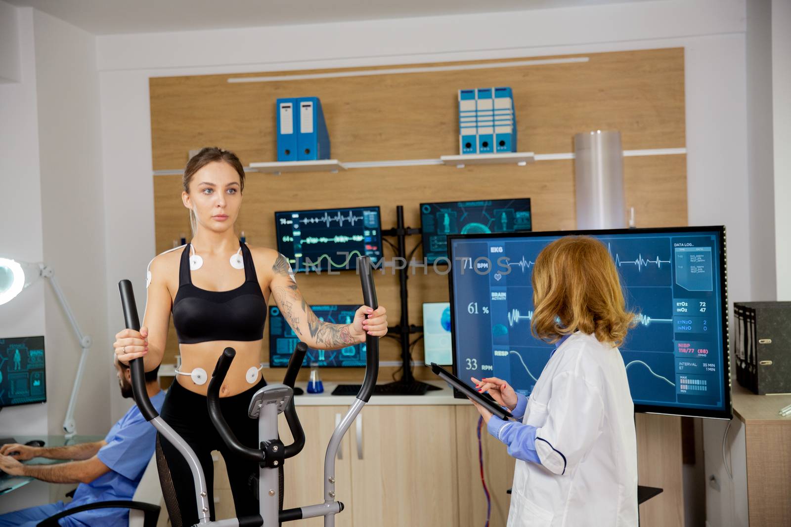 Fit female doing endurance test in the lab. Doctor makes notes in the tablet