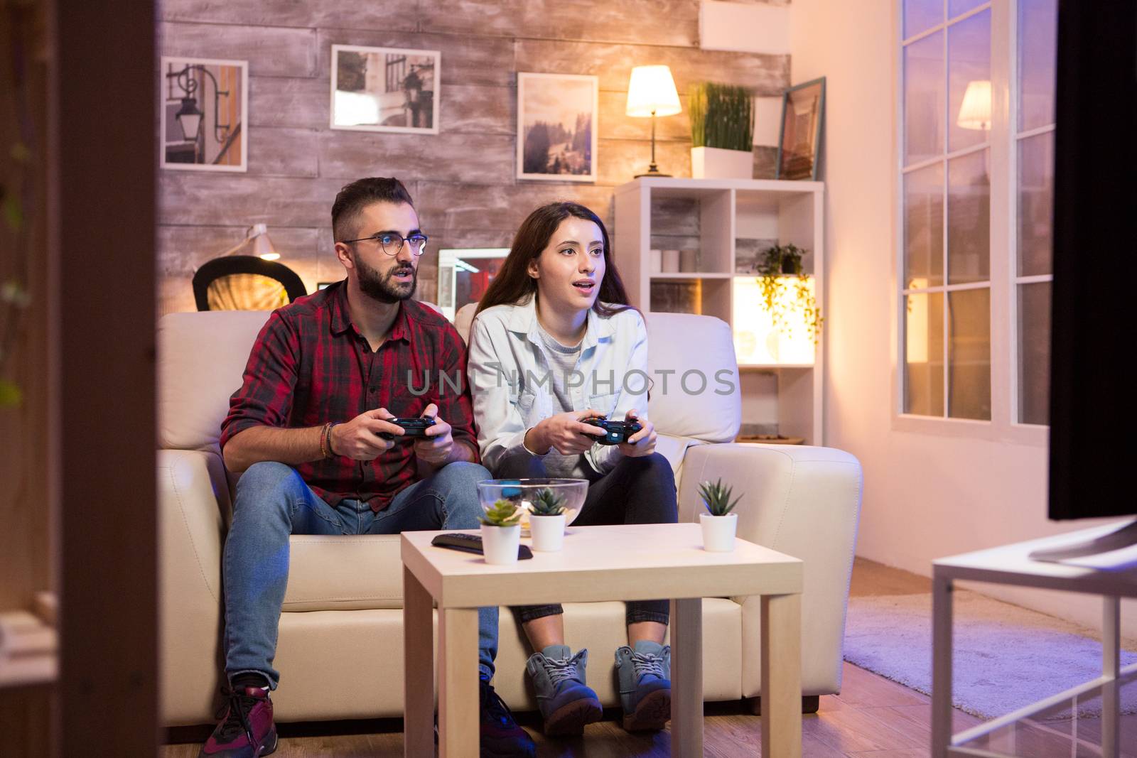 Young couple having a good time while playing video games on television. Couple sitting on sofa.