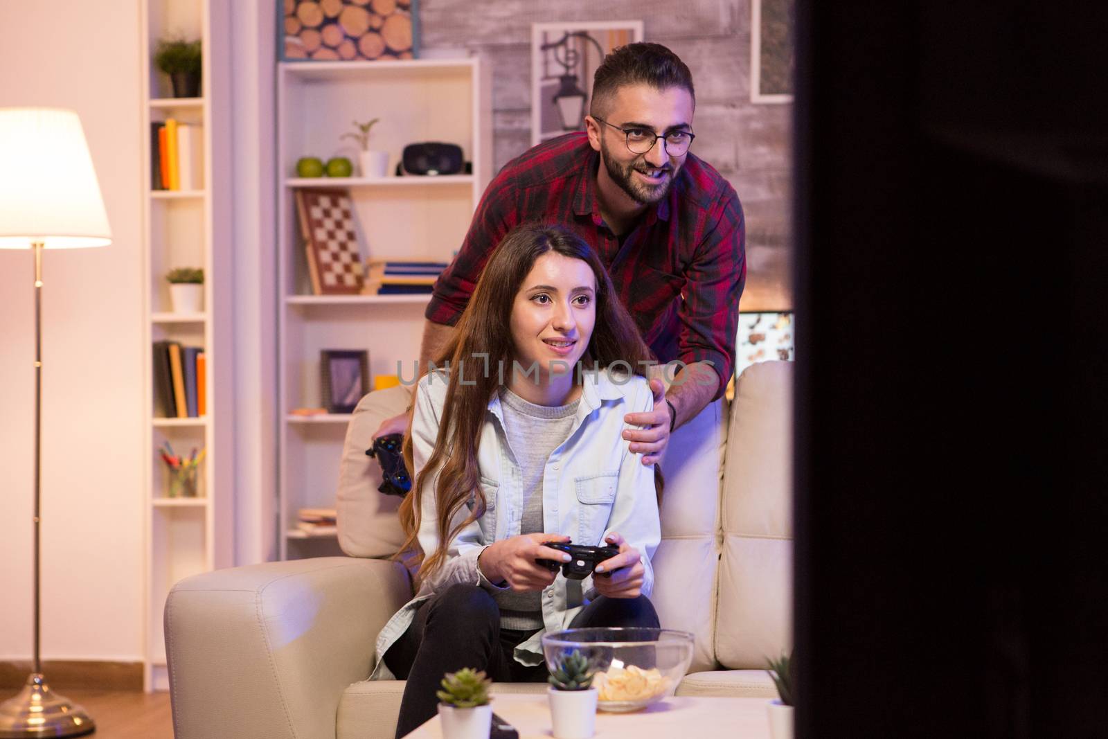 Happy young couple playing video games on television using controllers at night.
