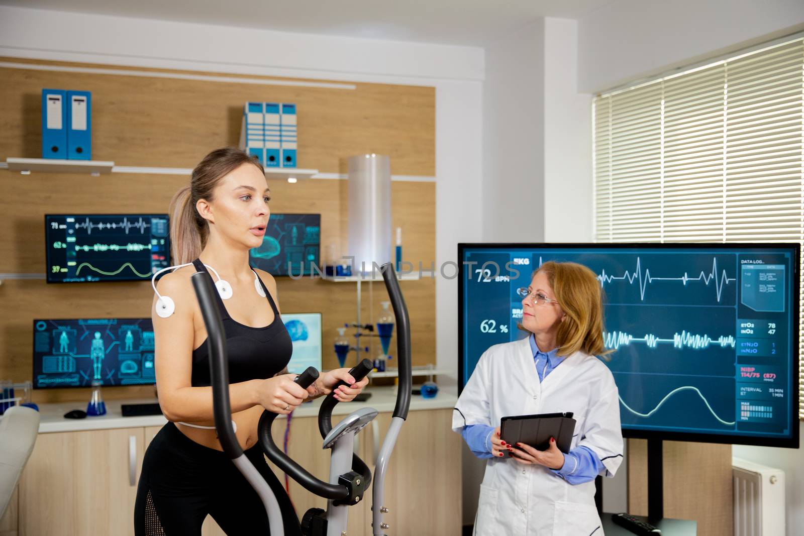 Female athlete testing the stepper with electrodes on her and the doctor follows her by DCStudio