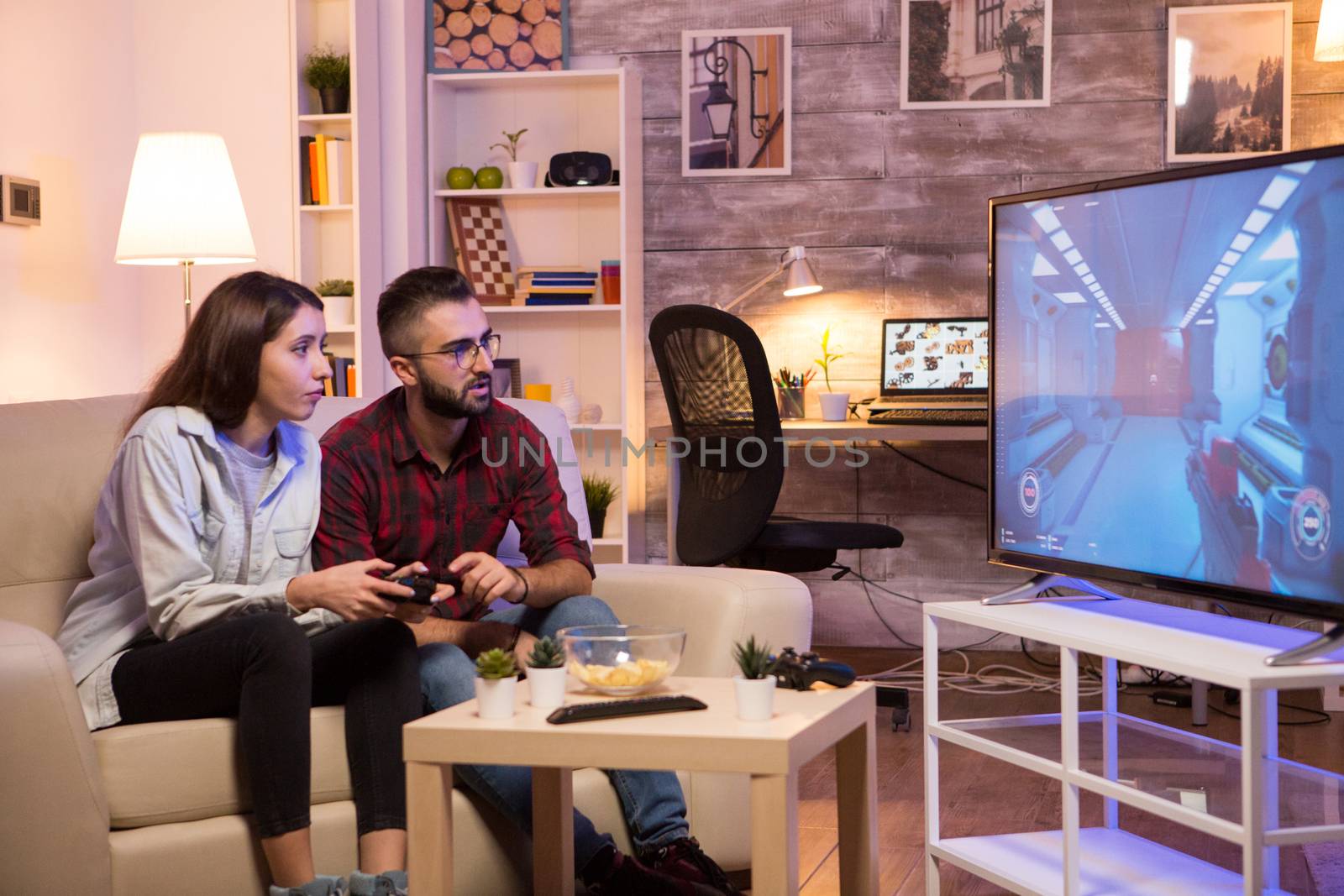 Boyfriend learning his girlfriend to play video games on television using controllers. Couple sitting on couch.