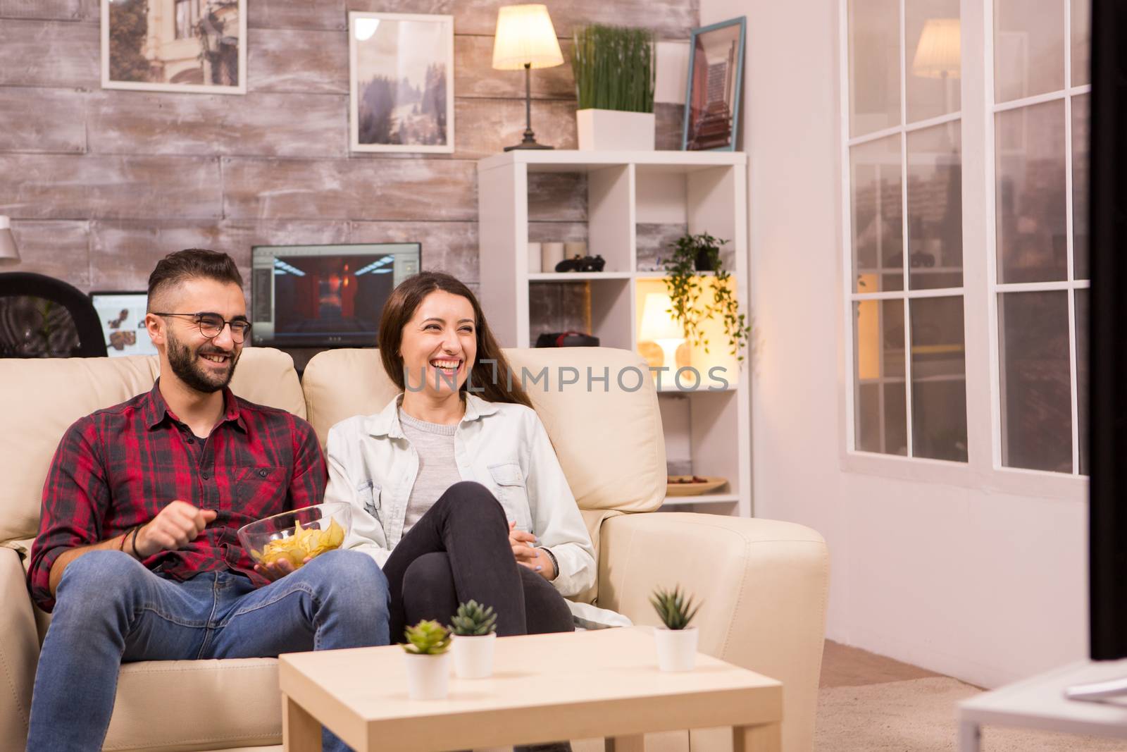 Couple laughing so hard while watching a movie on tv by DCStudio