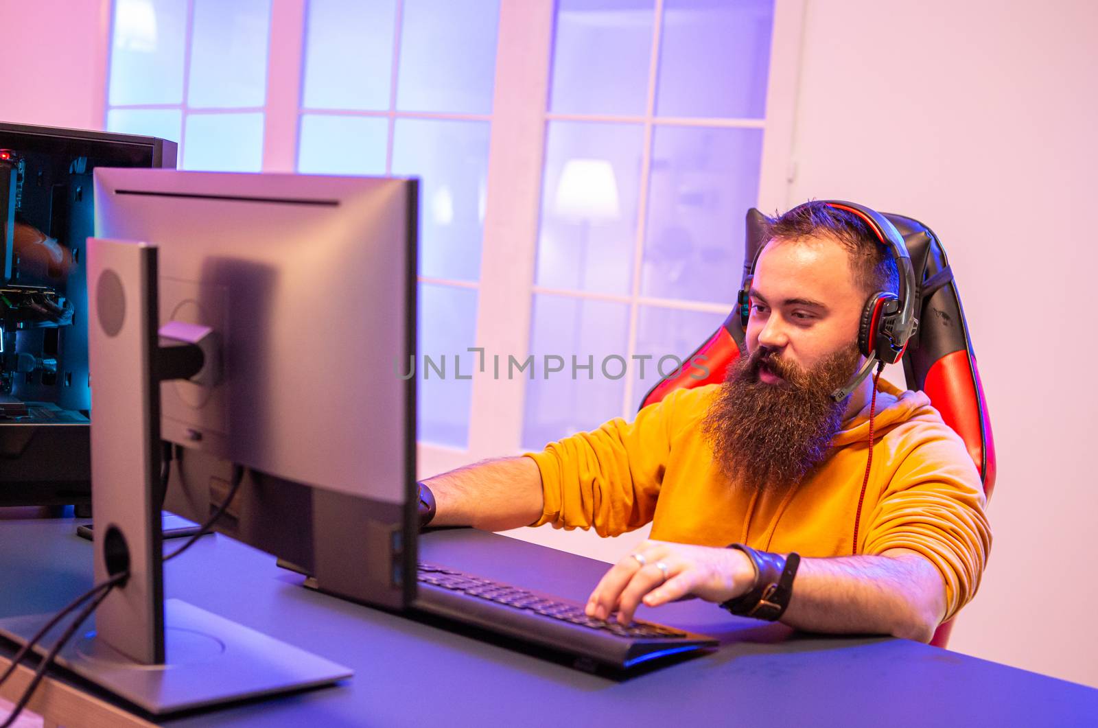 Hipster man playing professional video games in his room with colorful neons. Man wearing headphones while playing video games.