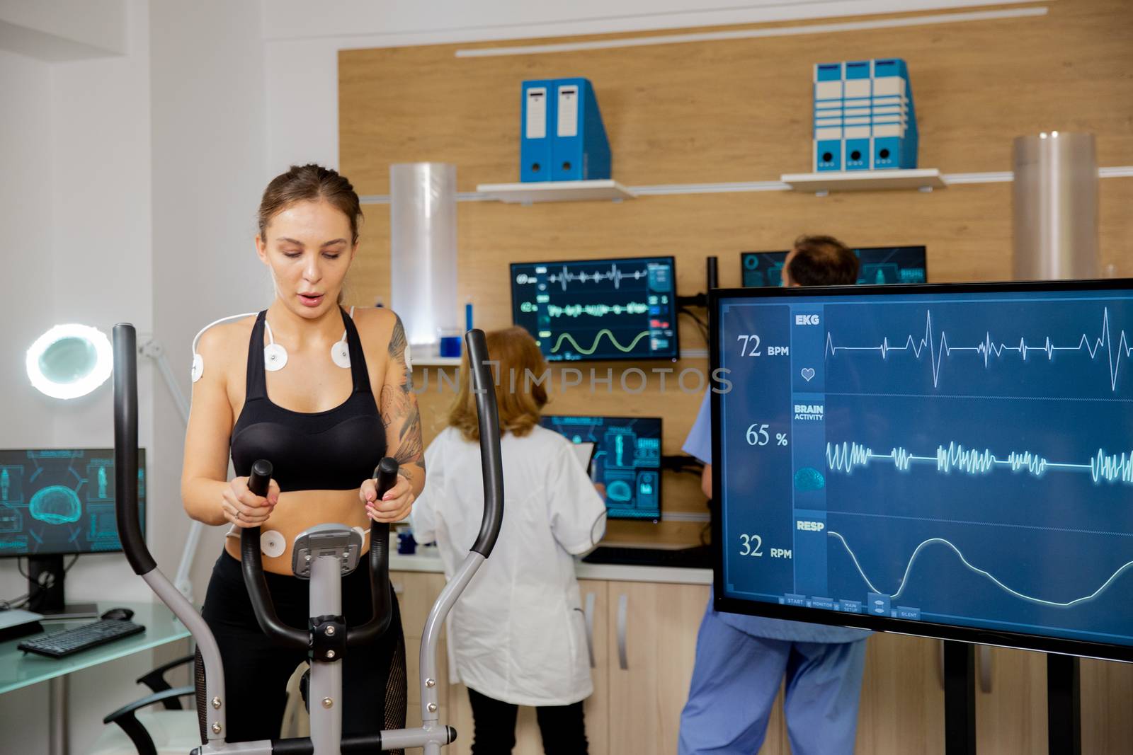 Female athlete who makes a physical effort on the stepper and has electrodes attached to it and her heartbeat pulses can be seen on the screen. Modern sports laboratory