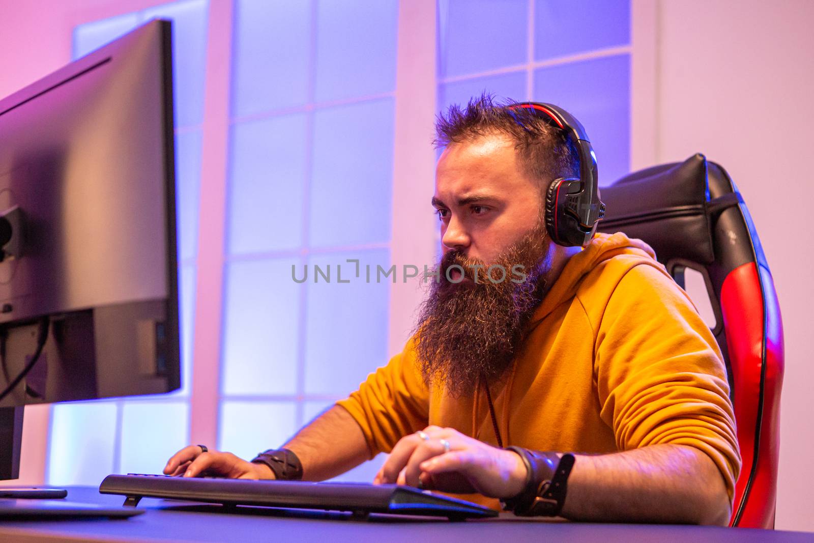 Professional gamer with long beard in front of powerful gaming rig in room full of neon lights