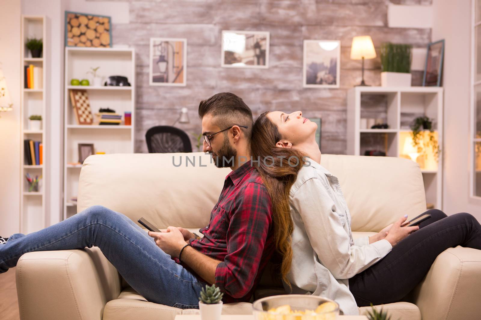 Upset couple sitting back to back on sofa in living room after a disagreement.