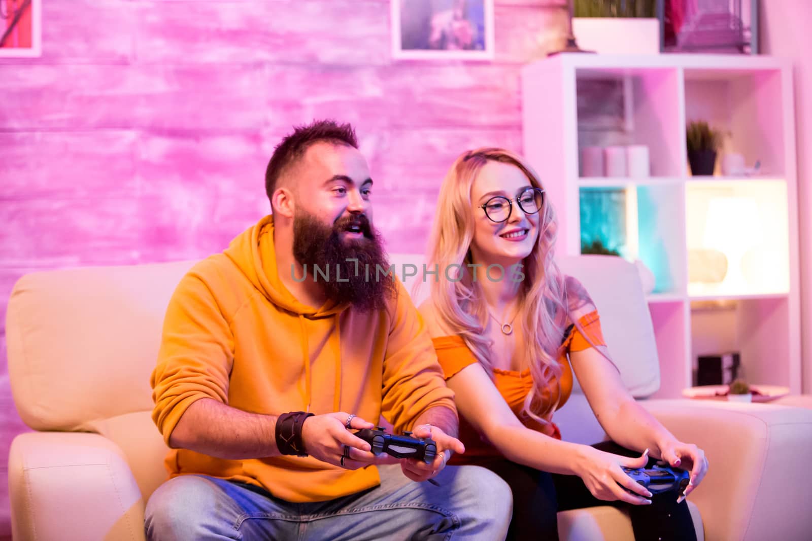 Older brother playing online games with his little sister in living room using wireless controller. Room with neon light.