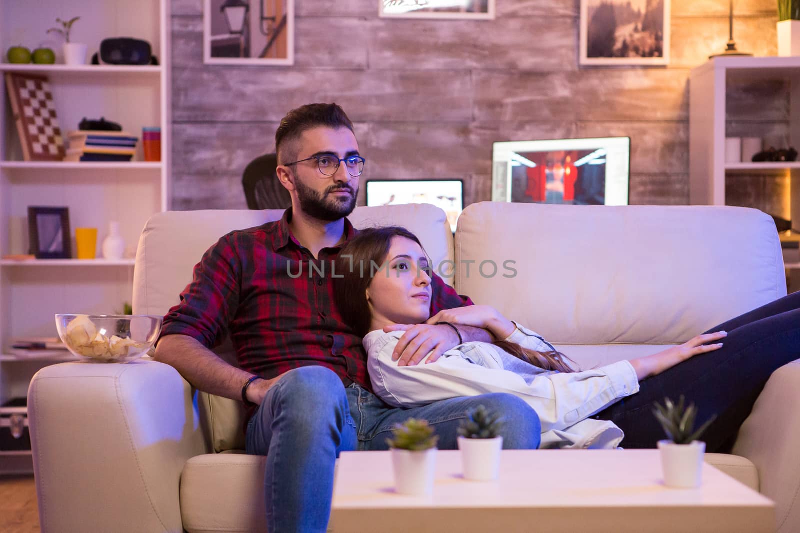 Beautiful young couple watching their favorite tv show while relaxing on couch at night.