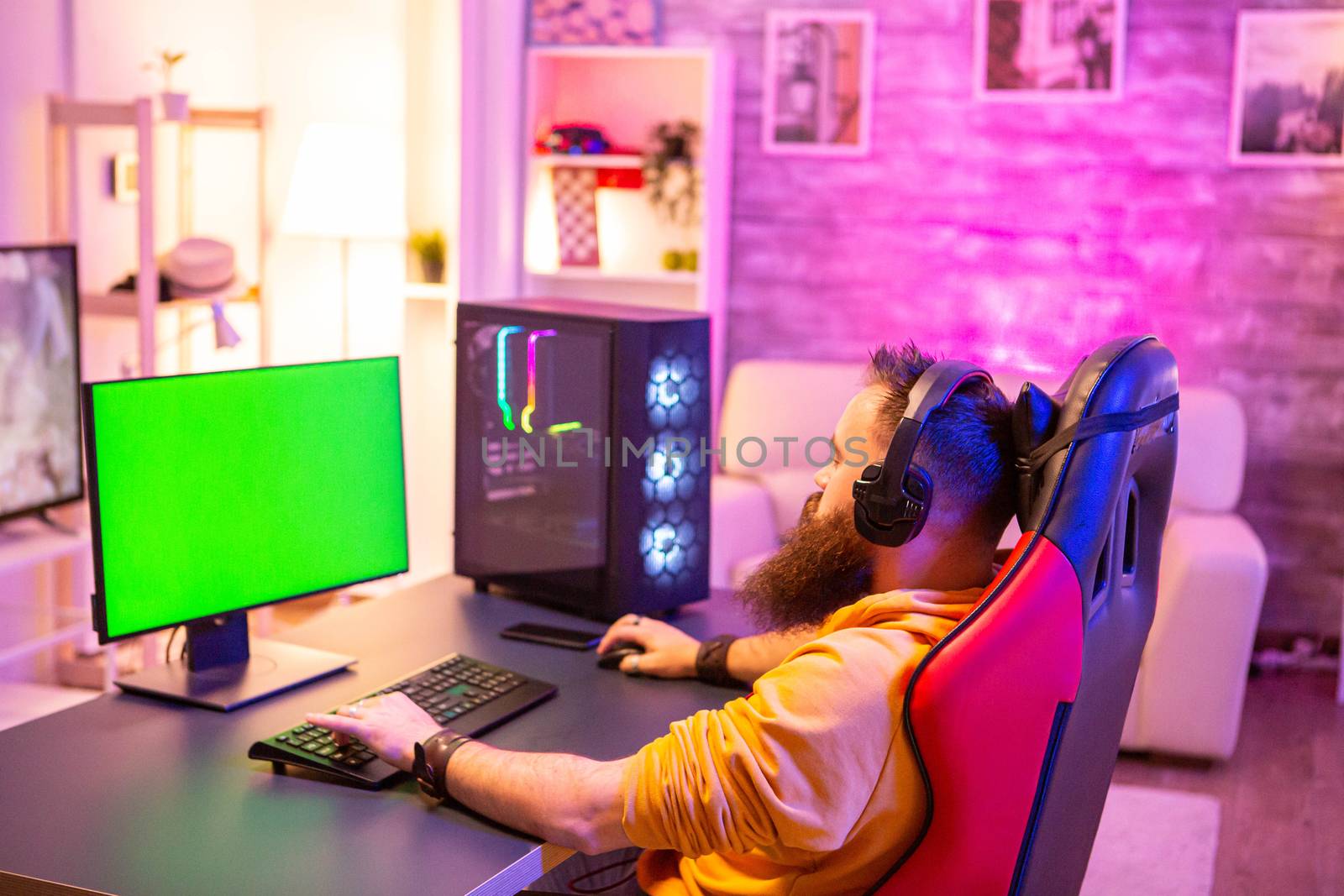 Man playing on powerfull gaming pc in a room with neon lights on a green screen computer.