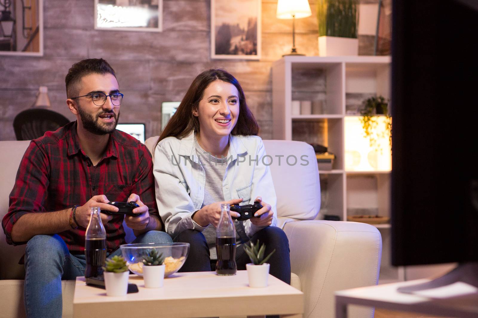 Cheerful couple playing video games at night using controllers. Couple sitting on couple.