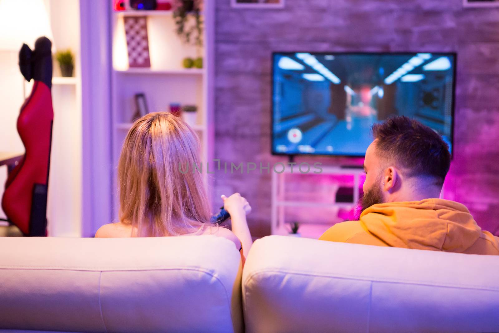 Young couple playing together online shooter games with wireless controllers. Couple playing videogames.