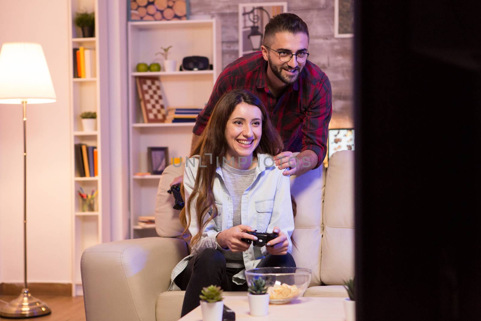 Happy young couple playing video games on television using controllers at night.