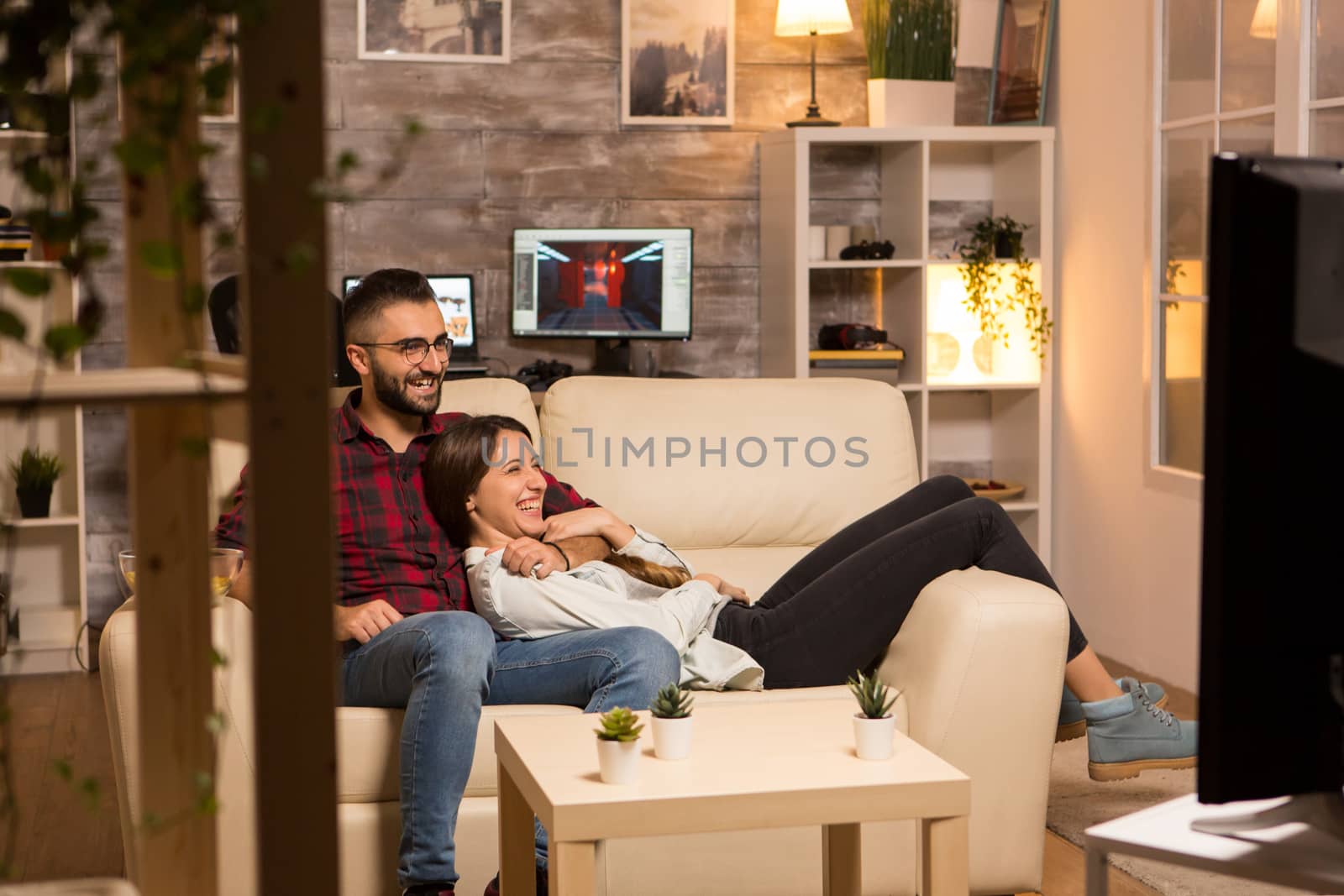 Lovely young couple relaxing on couch and watching a movie on tv at night.