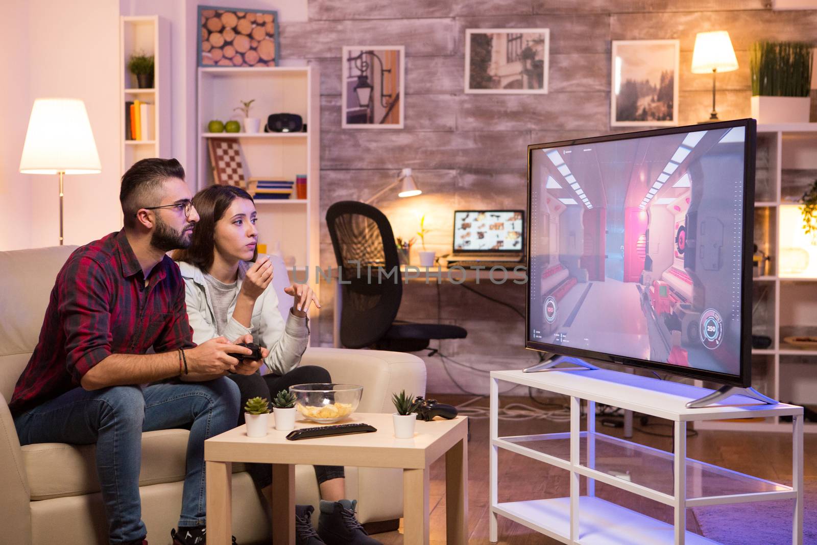 Man sitting on couch and playing video games on television while his girlfriend is eating chips.