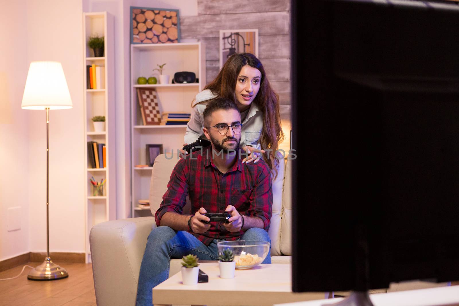 Young couple having fun while playing video games on televison sitting on couch at night.