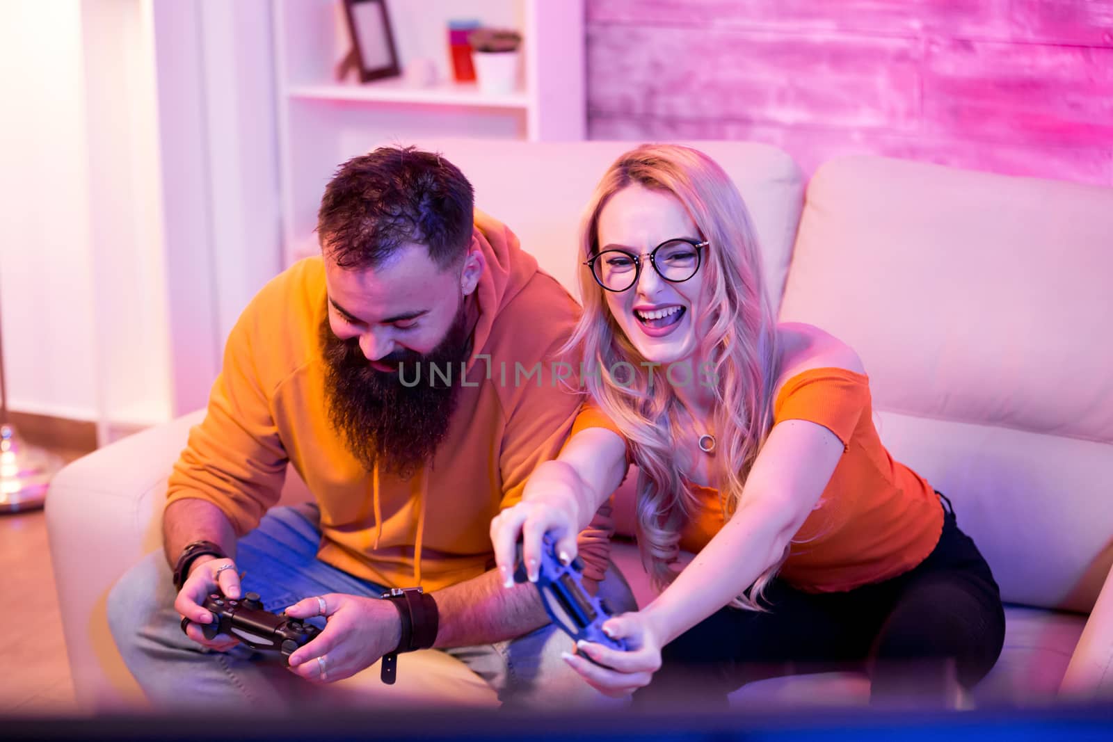 Beautiful young couple entertaining themselves playing online video games. Wireless controllers for gaming. Neon light
