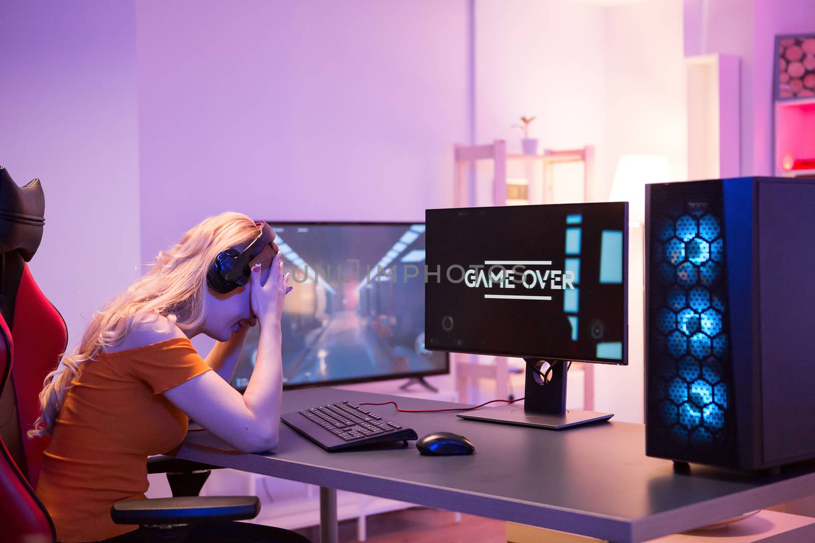 Disappointed beautiful girl because she lost while playing games on computer. Girl sitting on gaming chair. Game over.