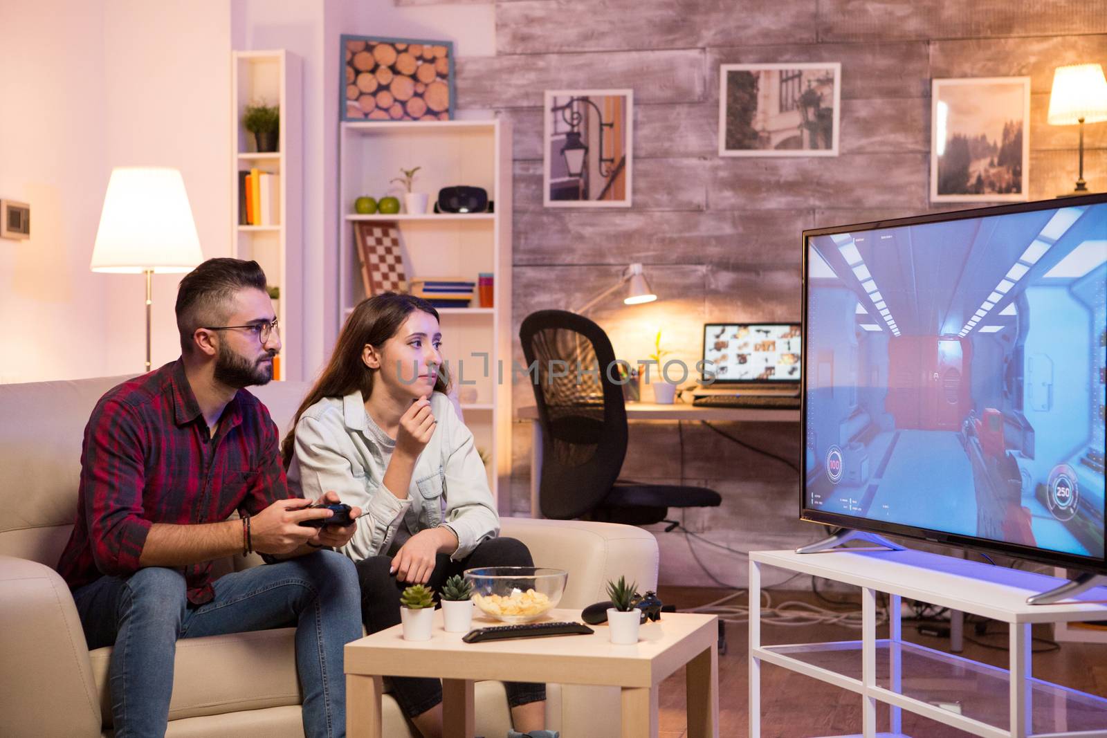 Man sitting on sofa next to his girlfriend and playing video games on television.