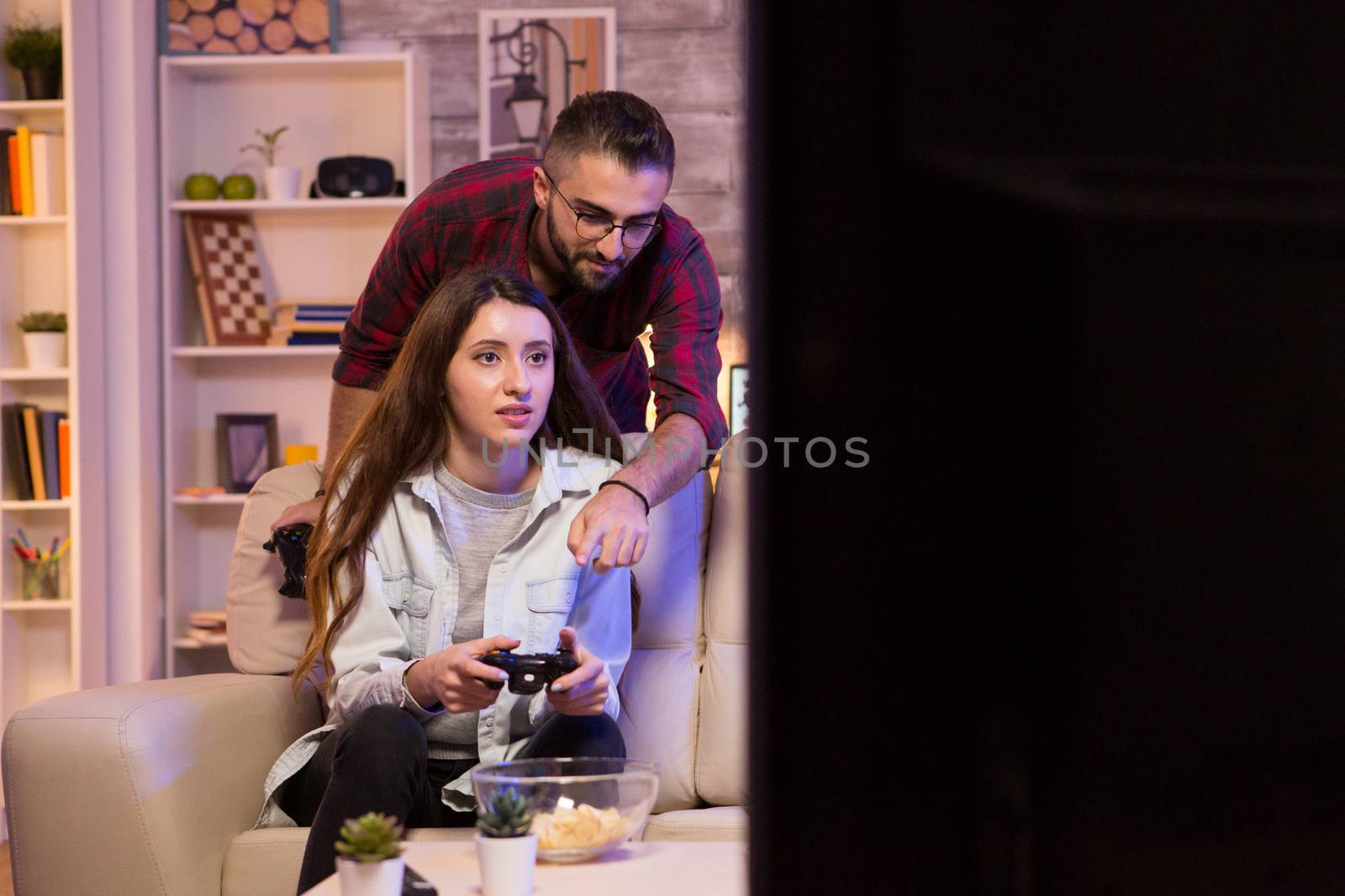 Boyfriend helping his girlfriend to play video games on television using controllers.