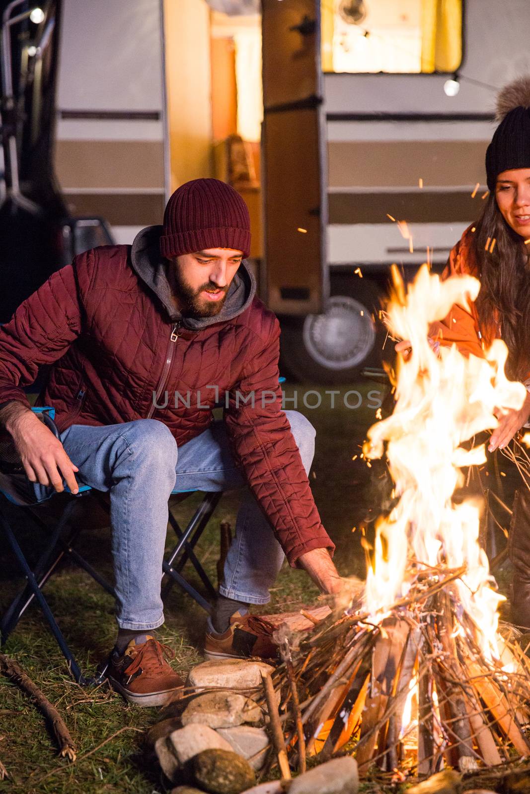 Man making the camp fire stronger in a cold night of autumn by DCStudio