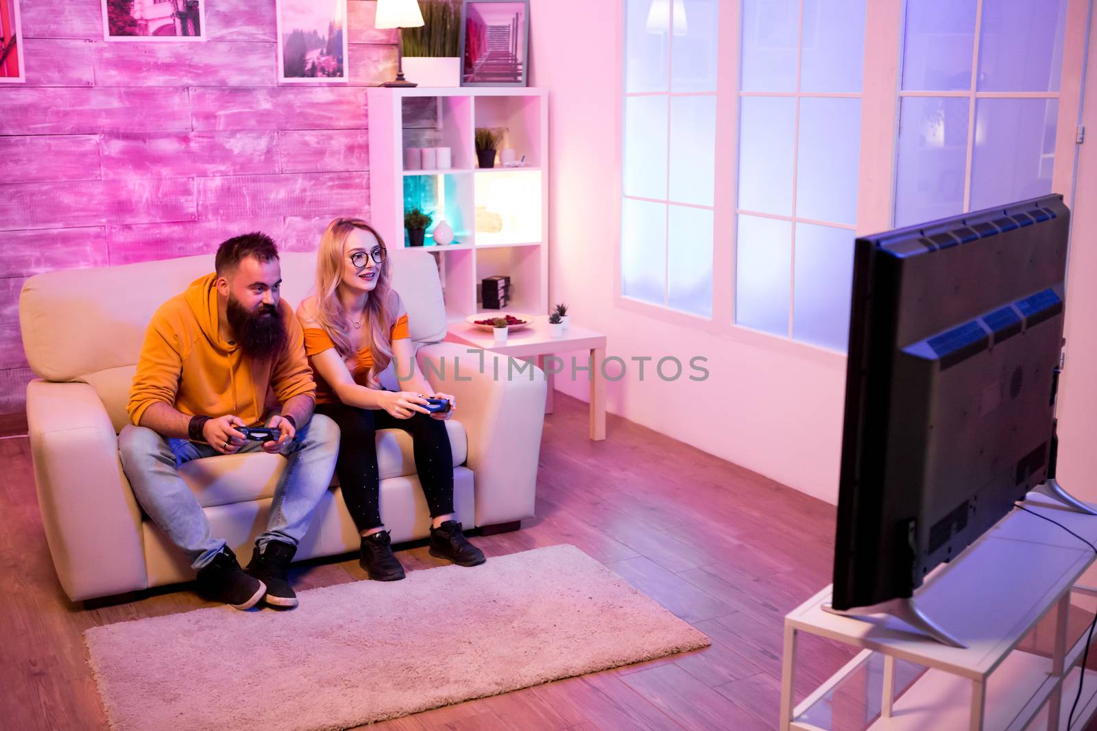 Beautiful young couple playing together online video games at home. Room with colorful neon lights.