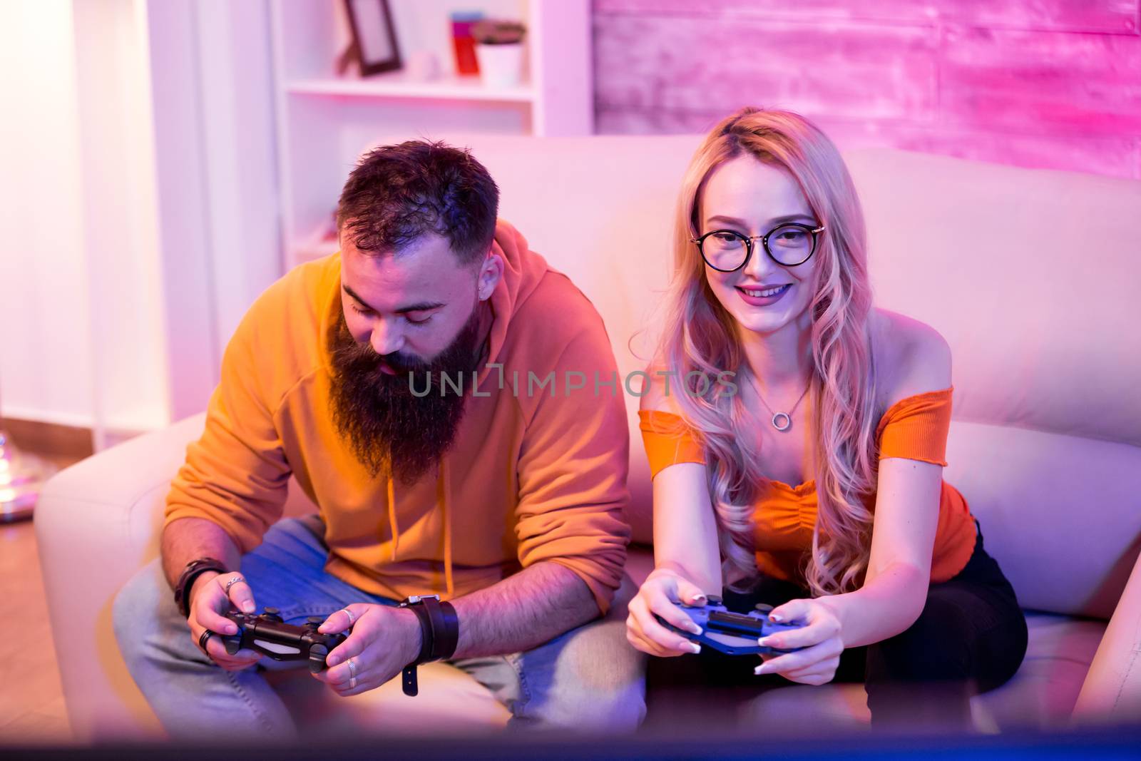 Cheerful young couple sitting on sofa and playing video games by DCStudio