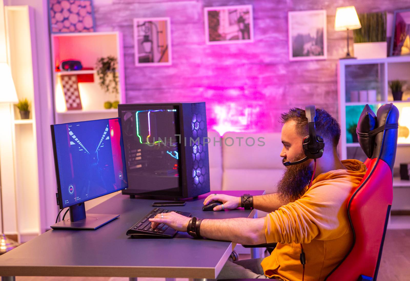 Hipster man playing professional video games in his room with colorful neons. Man wearing headphones while playing video games.