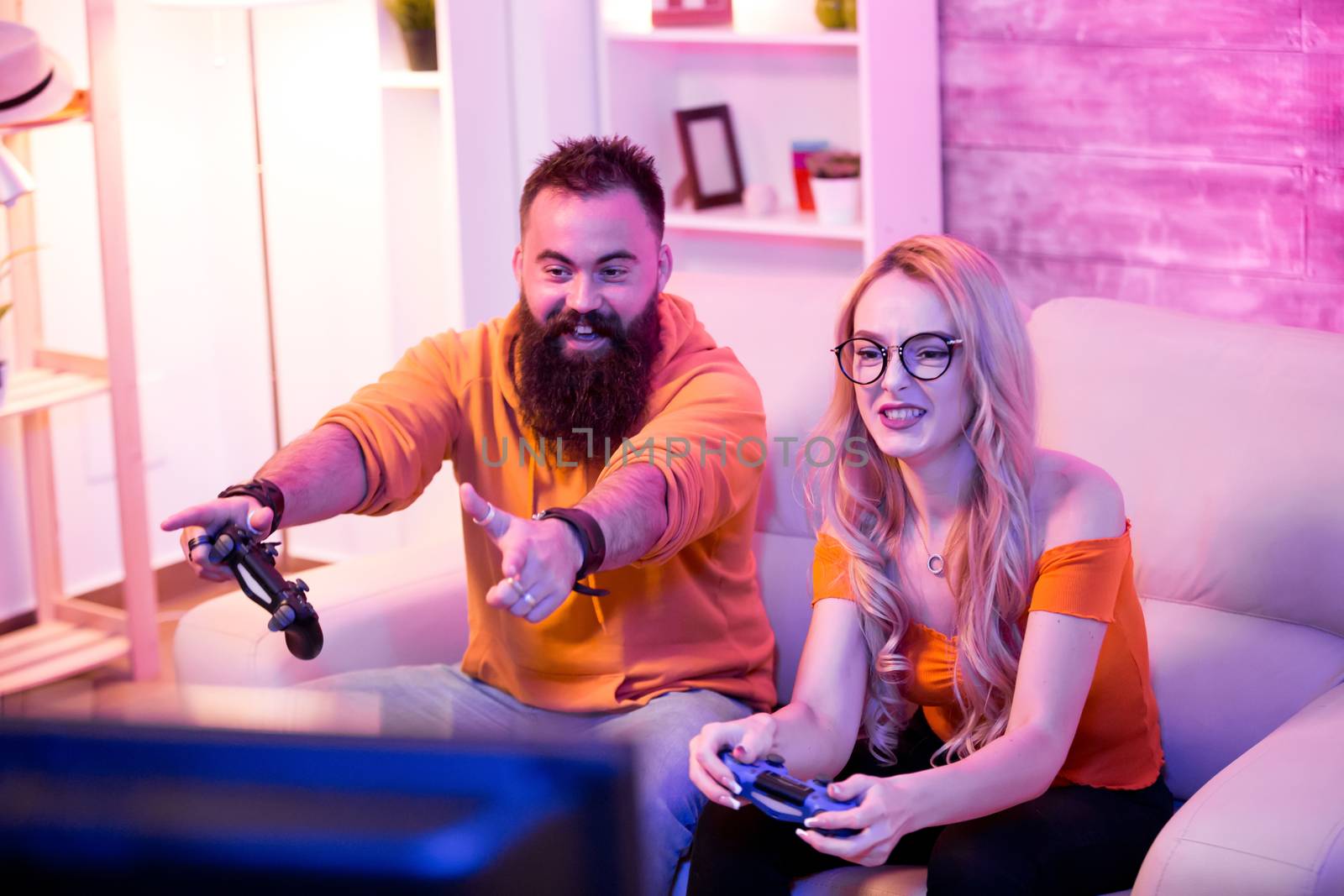 Boyfriend cheering her beautiul girlfriend while she's playing online games using wireless controller. Room with neon light.