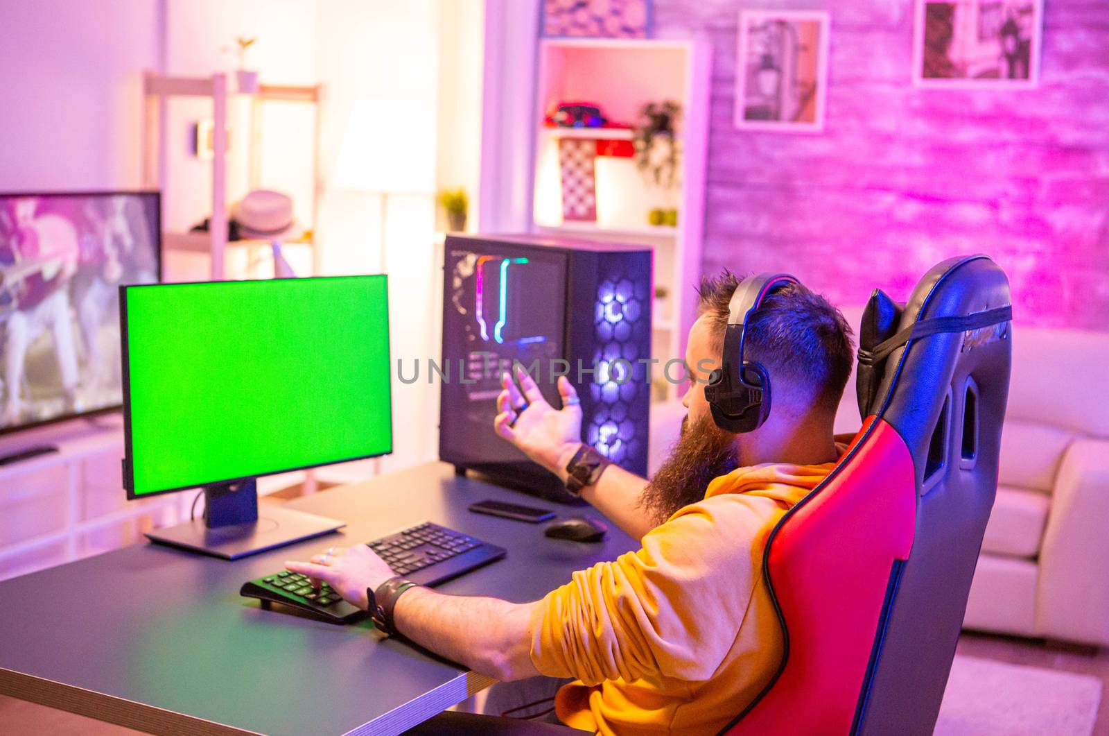 Man playing on powerfull gaming pc in a room with neon lights on a green screen computer.