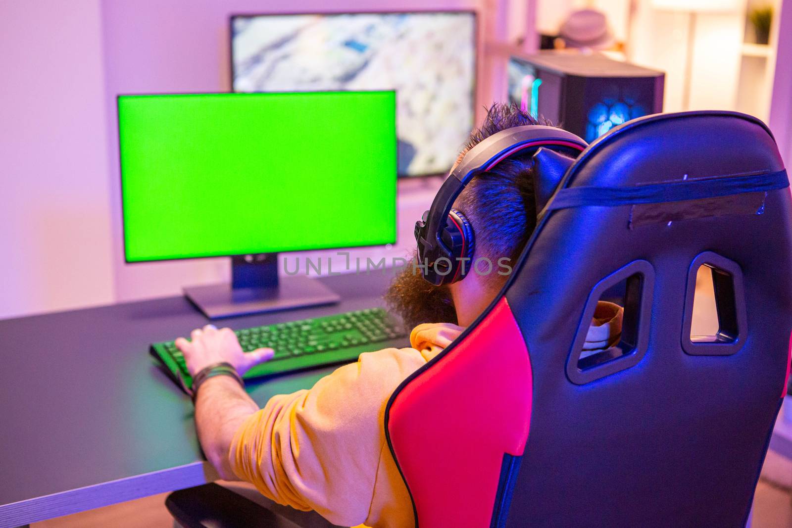 Man playing on powerfull gaming pc in a room with neon lights on a green screen computer.