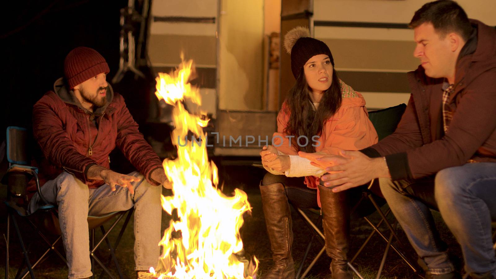 Handheld footage of friends warming their hand at camp fire in a cold autumn night. Retro camper van. Tourists enjoying fresh air.