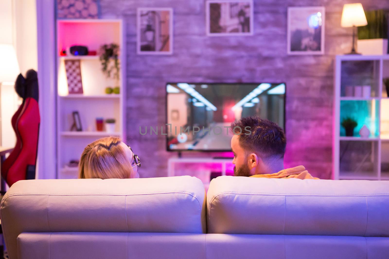 Back view of couple looking at each other while playing online video games on console in a room with neon light.