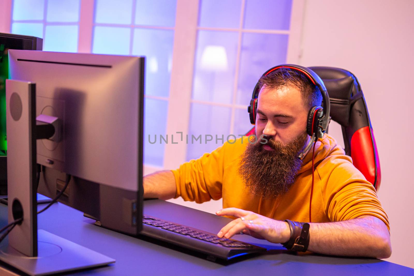 Hipster man playing professional video games in his room with colorful neons. Man wearing headphones while playing video games.