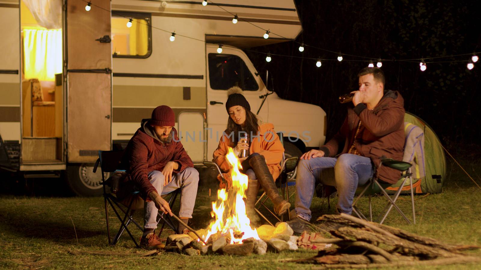 Group of friends enjoying a quiet moment in front of the fire in a camp at night