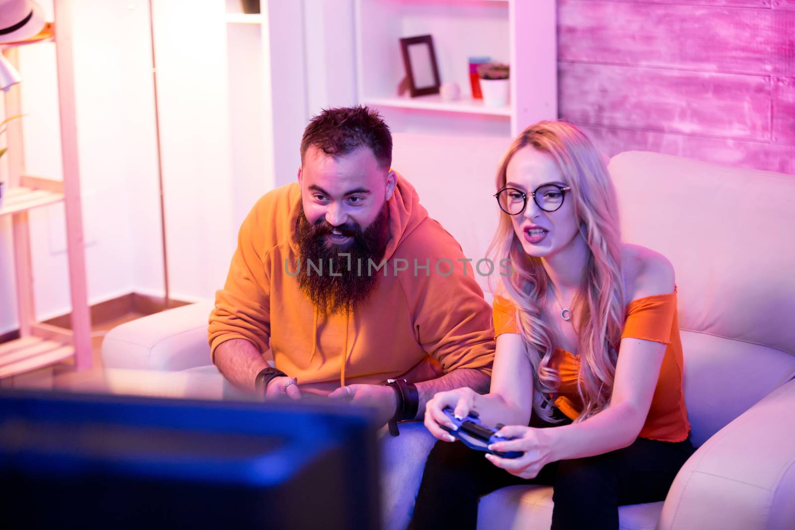 Excited young couple playing online video games together sitting on sofa. Couple using wireless joysticks. Focused female.