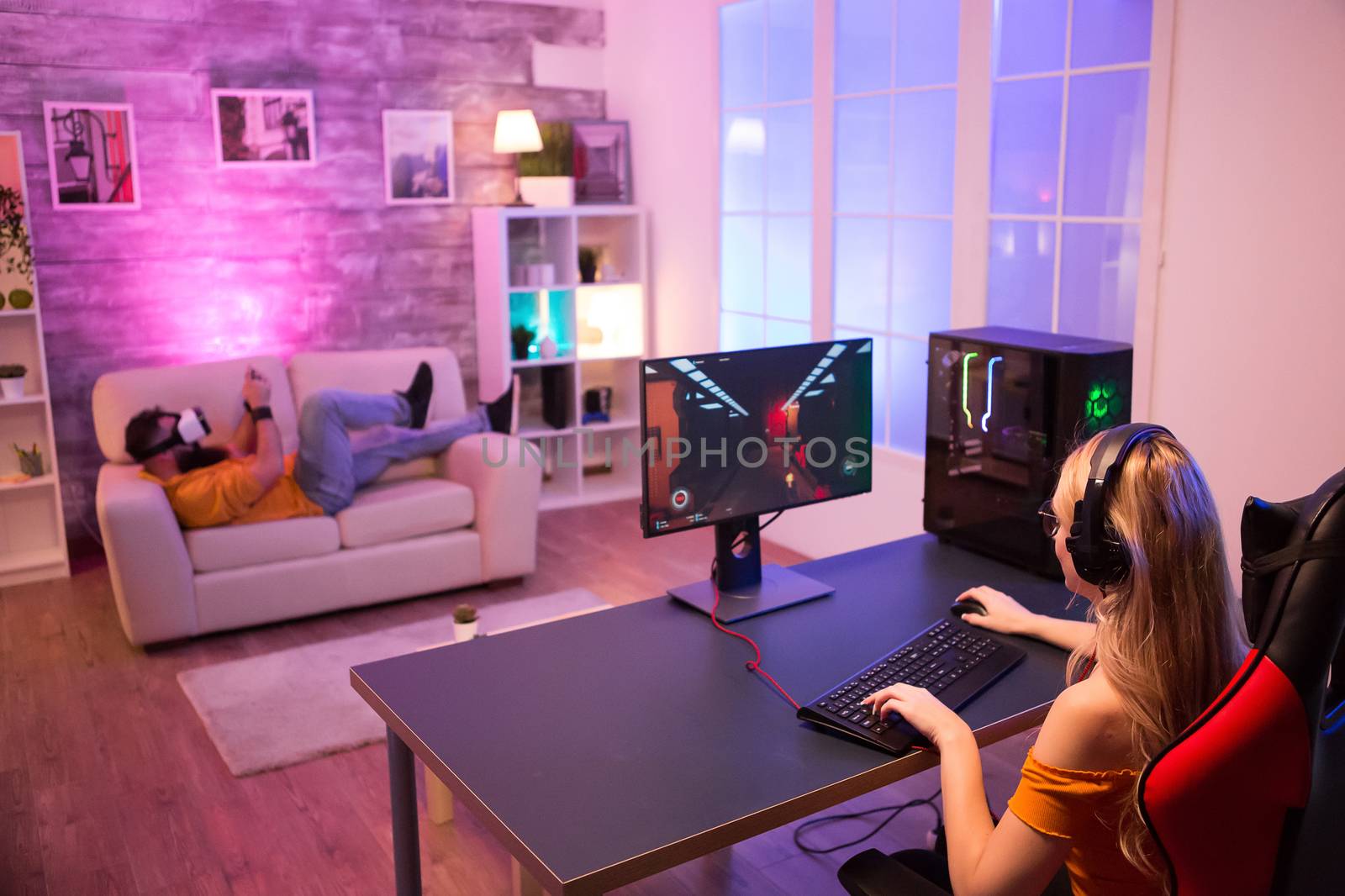 Couple relaxing while playing different games in a room with colorful neon light. Back view. Gaming chair.
