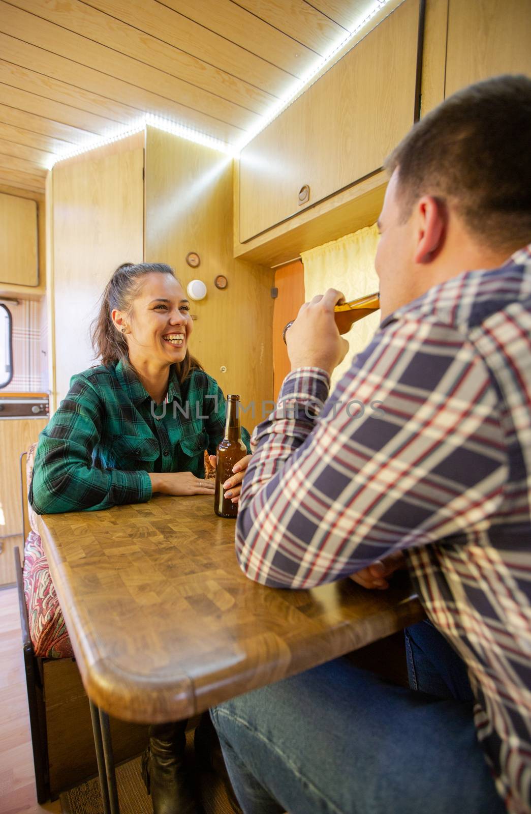 Loving couple smiling and chatting while drinking beer in the caravan. Vacation together