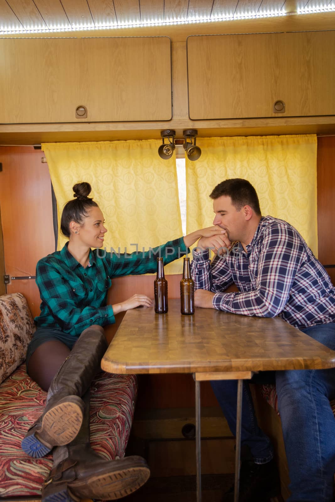 Boyfriend kissing his girlfriend's hand is sitting at the table in the retro camper. Holiday together