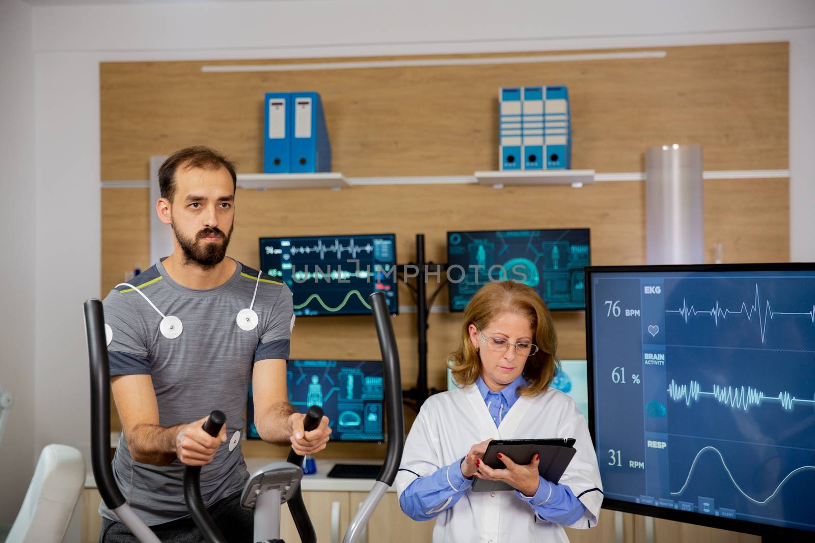 Male athlete who makes a physical effort on the stepper and has electrodes attached to him and the doctor who follows the tablet and makes notes. Hard sports tests