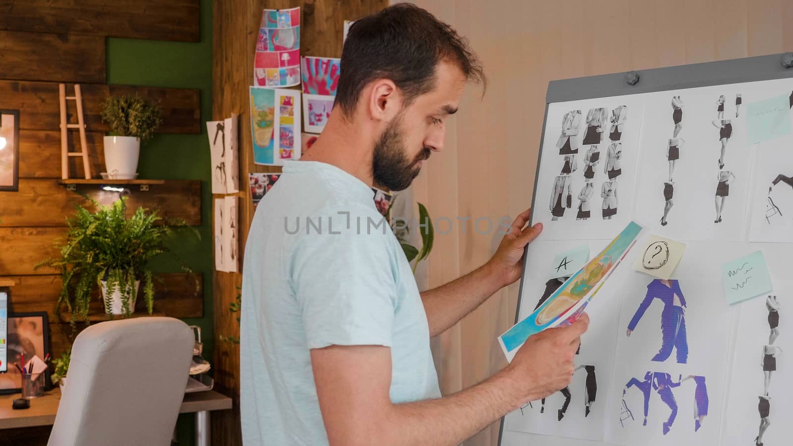 The designer boy looks at a printed picture that he holds in his hand near a whiteboard. Creative agency and modern office