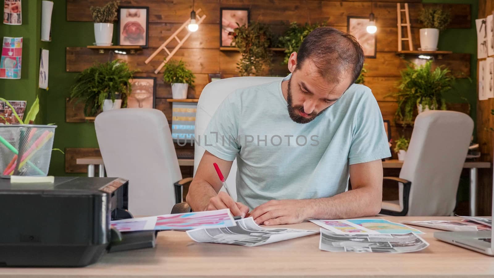 Designer boy who sits at the desk and makes some notes on some printed sheets. Loft office