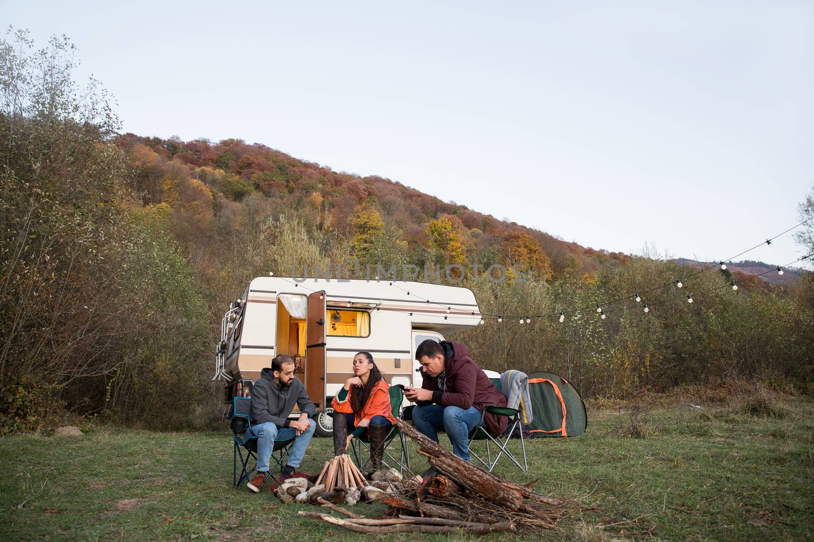 Group of friends camping together in the mountains wainting for the night to make camp fire. Retro camper van.